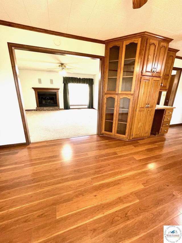 unfurnished living room with a ceiling fan, a fireplace with raised hearth, crown molding, and wood finished floors