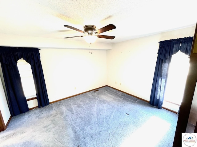 carpeted empty room with a textured ceiling, baseboards, and a ceiling fan