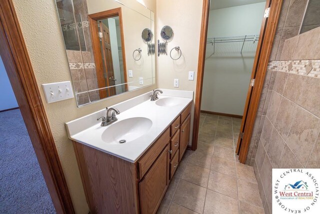 bathroom with a walk in closet, tile patterned floors, a sink, and double vanity