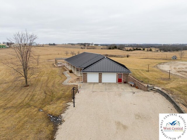 view of front of home featuring brick siding, metal roof, a garage, a rural view, and driveway