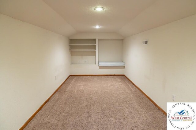 carpeted empty room with visible vents, vaulted ceiling, and baseboards