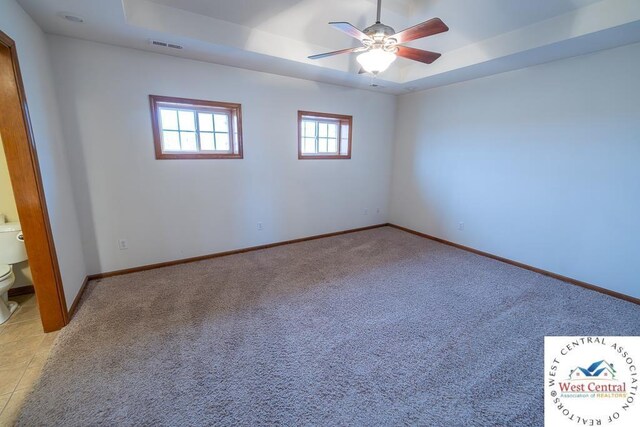 spare room featuring light colored carpet, a raised ceiling, visible vents, and baseboards