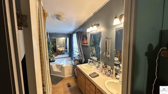 full bathroom featuring visible vents, a garden tub, a textured ceiling, wood finished floors, and double vanity