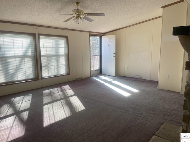 carpeted spare room with a textured ceiling, ceiling fan, visible vents, and crown molding