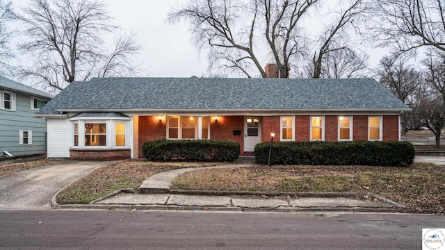 ranch-style house featuring brick siding, roof with shingles, and a chimney