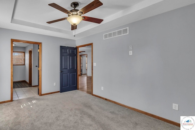 unfurnished bedroom featuring ceiling fan, visible vents, baseboards, a tray ceiling, and carpet