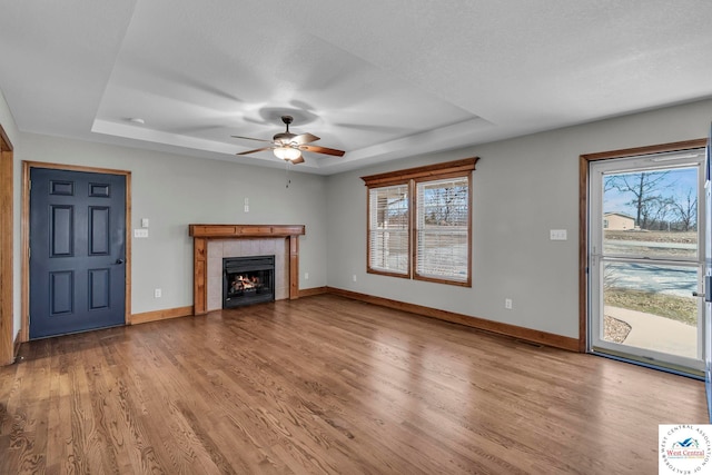 unfurnished living room with light wood-style flooring, baseboards, a raised ceiling, and a tile fireplace