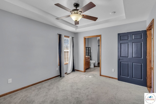 unfurnished bedroom featuring a tray ceiling, light colored carpet, a ceiling fan, ensuite bath, and baseboards