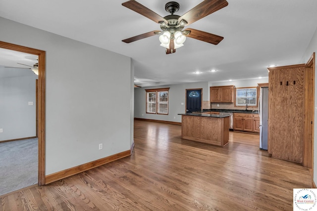 kitchen with a sink, baseboards, light wood-style floors, appliances with stainless steel finishes, and dark countertops