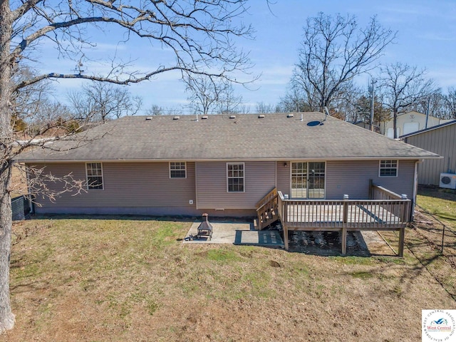 back of property with a deck, roof with shingles, and a lawn