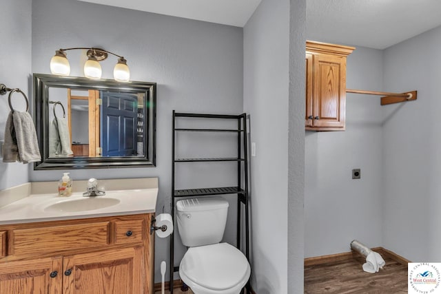 half bathroom featuring baseboards, vanity, toilet, and wood finished floors