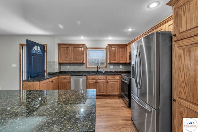 kitchen with a sink, appliances with stainless steel finishes, light wood-type flooring, backsplash, and brown cabinets