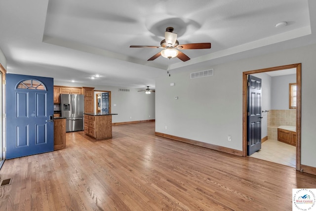 unfurnished living room featuring light wood-type flooring, visible vents, and a tray ceiling