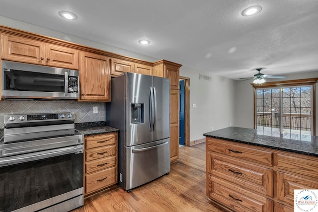 kitchen with visible vents, backsplash, appliances with stainless steel finishes, brown cabinetry, and light wood-type flooring