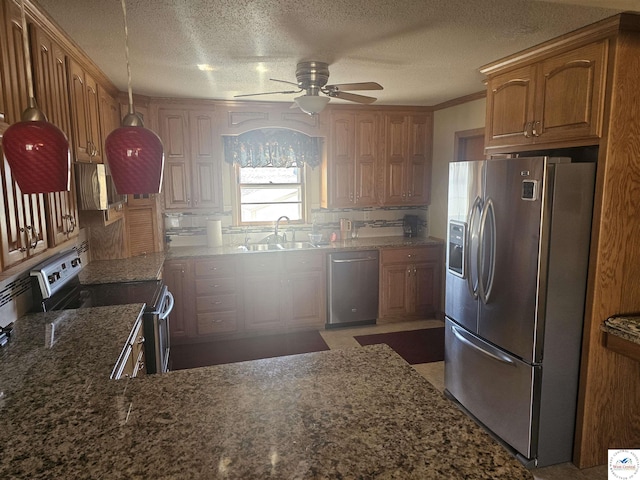 kitchen featuring dark stone counters, a sink, appliances with stainless steel finishes, a textured ceiling, and brown cabinets