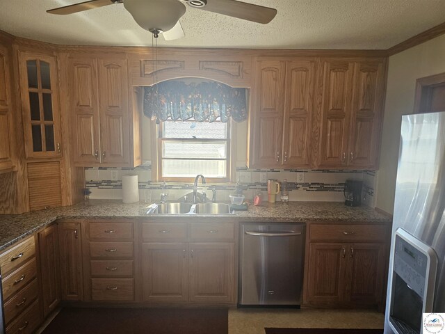 kitchen with brown cabinetry, light stone countertops, a ceiling fan, a sink, and appliances with stainless steel finishes