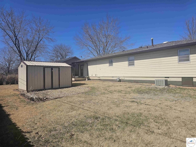 rear view of property with an outbuilding, a lawn, a storage shed, and central AC