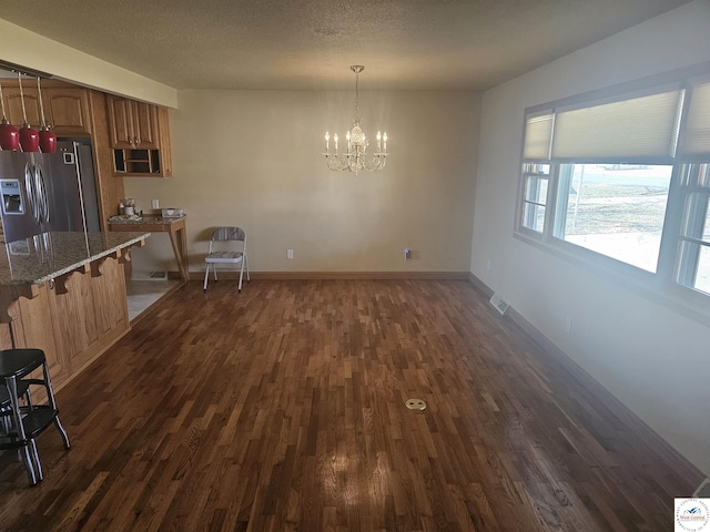 unfurnished dining area with visible vents, dark wood-type flooring, a notable chandelier, a textured ceiling, and baseboards