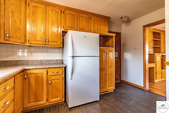 kitchen with backsplash, baseboards, brown cabinets, freestanding refrigerator, and dark wood-style flooring