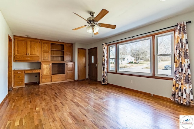 unfurnished living room featuring built in desk, light wood-style flooring, baseboards, and ceiling fan