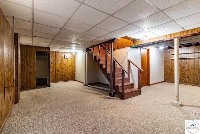 finished below grade area featuring wooden walls, baseboards, carpet, stairway, and a drop ceiling