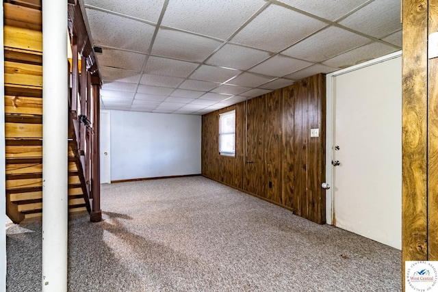 basement with a paneled ceiling, carpet, and wood walls