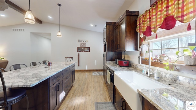 kitchen with light stone counters, a breakfast bar, vaulted ceiling with beams, visible vents, and a sink