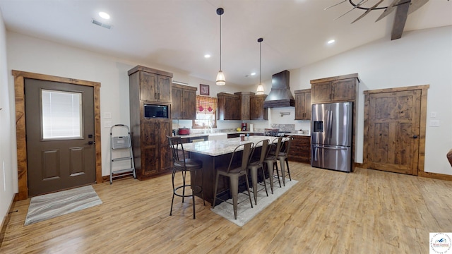 kitchen with stainless steel fridge, visible vents, a kitchen island, decorative light fixtures, and custom exhaust hood