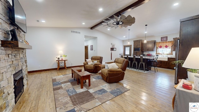 living area featuring a stone fireplace, visible vents, lofted ceiling with beams, and light wood finished floors