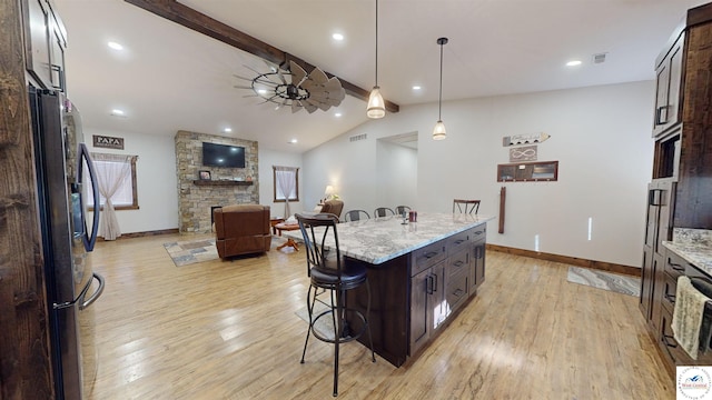 kitchen featuring light stone counters, a breakfast bar, a fireplace, freestanding refrigerator, and pendant lighting