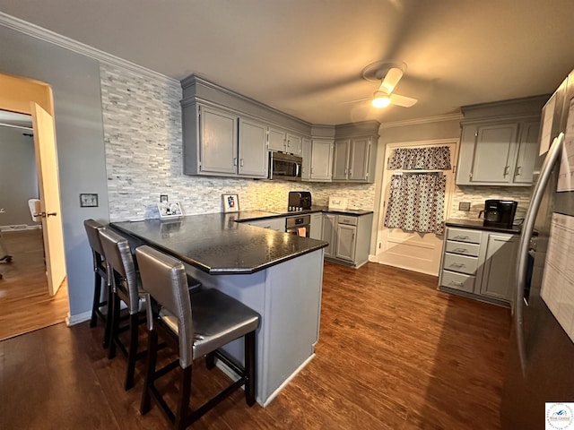 kitchen with crown molding, dark countertops, stainless steel microwave, gray cabinetry, and a peninsula