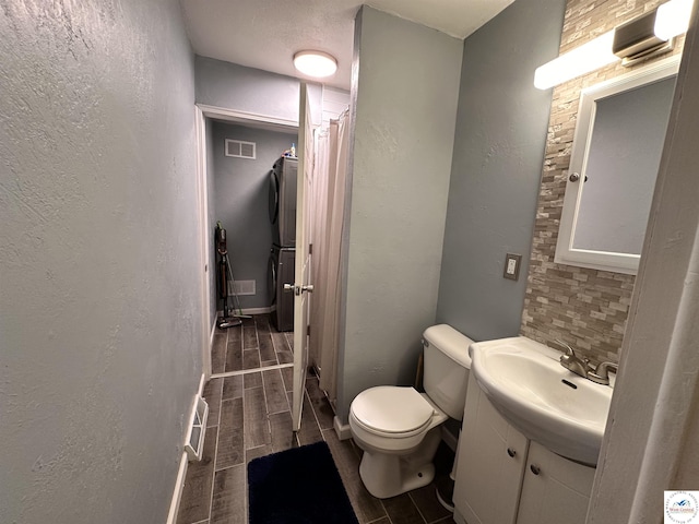 bathroom with toilet, a textured wall, vanity, and visible vents