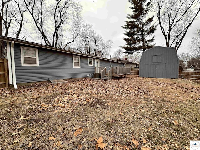 rear view of house featuring a storage unit, central AC unit, fence, a deck, and an outdoor structure