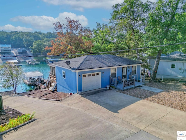 ranch-style home with an attached garage, covered porch, a water view, concrete driveway, and roof with shingles