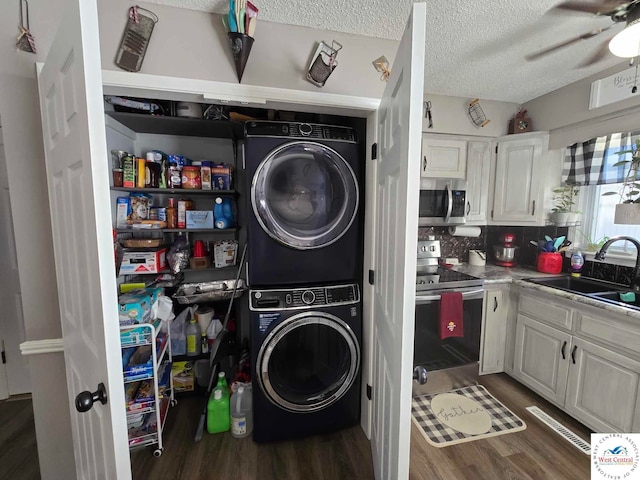 laundry room featuring dark wood-style floors, stacked washer / drying machine, a sink, a textured ceiling, and laundry area