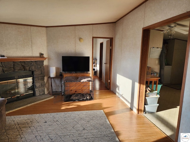 living area featuring light wood-style floors, a fireplace, ceiling fan, and ornamental molding