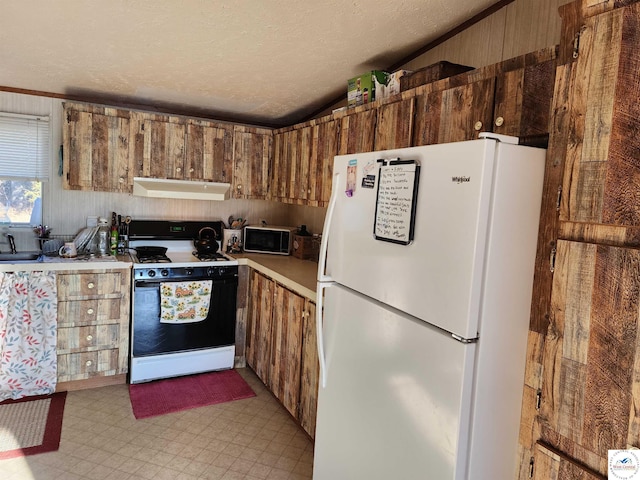 kitchen with wooden walls, under cabinet range hood, light countertops, freestanding refrigerator, and gas range