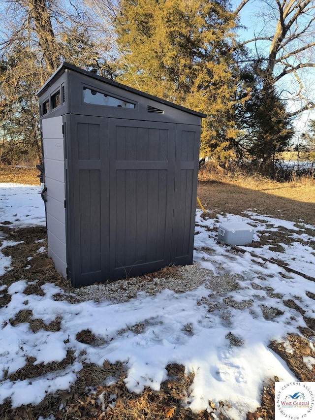 snow covered structure featuring a storage shed and an outbuilding