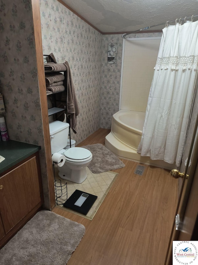 bathroom featuring a textured ceiling, toilet, wood finished floors, a bathtub, and wallpapered walls