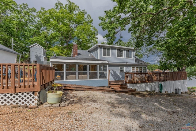 rear view of property featuring a sunroom, a chimney, and a wooden deck