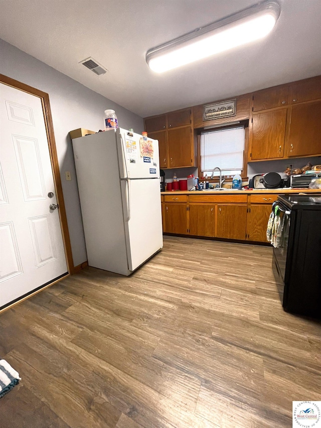 kitchen featuring black range with electric stovetop, visible vents, freestanding refrigerator, light wood finished floors, and brown cabinetry