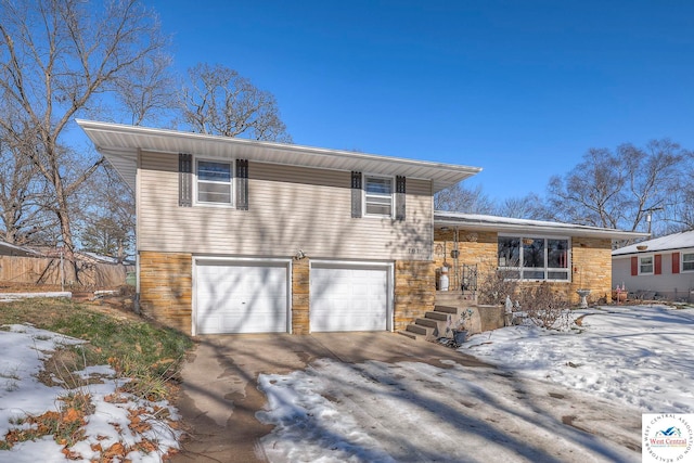 split level home with an attached garage, stone siding, and concrete driveway