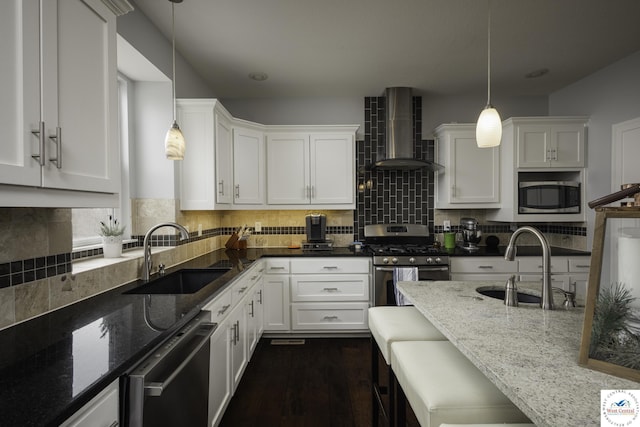 kitchen featuring dark stone counters, wall chimney exhaust hood, stainless steel appliances, and a sink