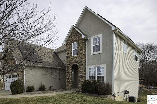 traditional home featuring a front lawn, an attached garage, stone siding, and stucco siding