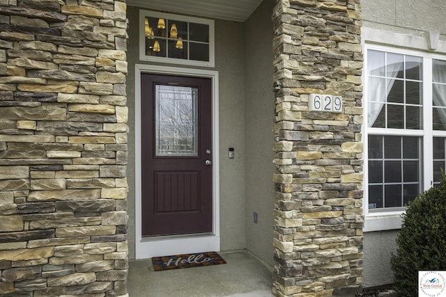 view of exterior entry featuring stone siding and stucco siding