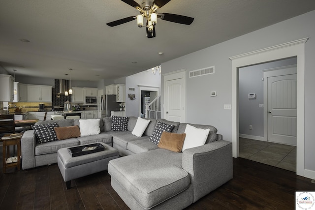 living area featuring stairway, dark wood-style floors, baseboards, visible vents, and ceiling fan