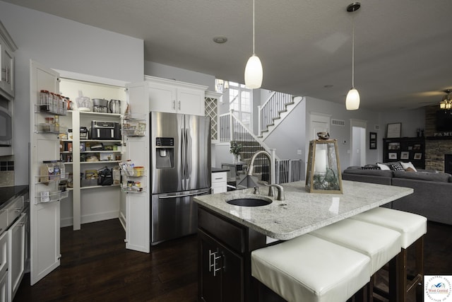 kitchen with dark wood-type flooring, a sink, light stone counters, stainless steel fridge, and a fireplace