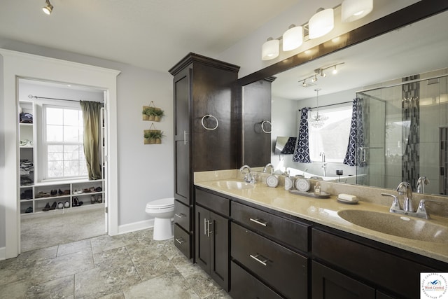 bathroom featuring a shower stall, double vanity, baseboards, and a sink