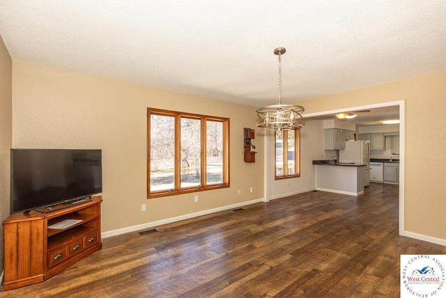 unfurnished living room with dark wood finished floors, an inviting chandelier, baseboards, and visible vents