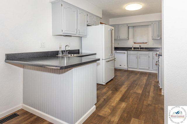 kitchen featuring dark countertops, visible vents, a peninsula, white appliances, and a sink